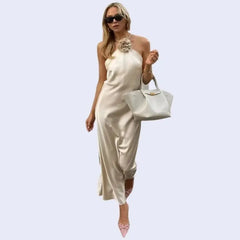 Mannequin portant une robe longue épaules dénudées col haler avec fleur en satin couleur champagne